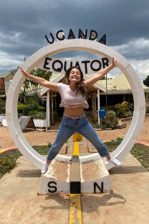 Capri Gutierrez jumping in front of Uganda/Equator sign