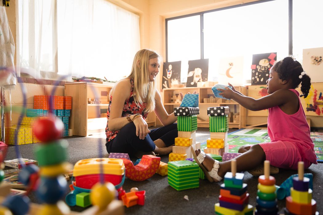 A behavior analysts works with a student stacking brightly colored blocks.