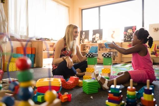 A behavior analyst sits on the floor and plays with a child. 