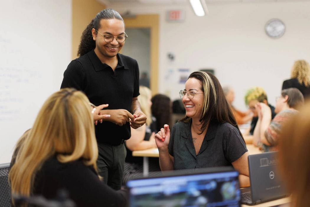 Three adult college students laugh during class.