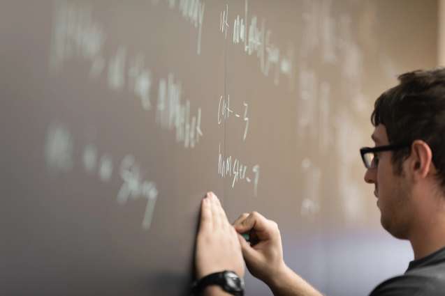 A computer science college student writing out ideas on a chalkboard for a local hackathon.