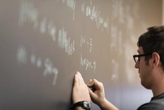 A computer science student writes out code on a blackboard.