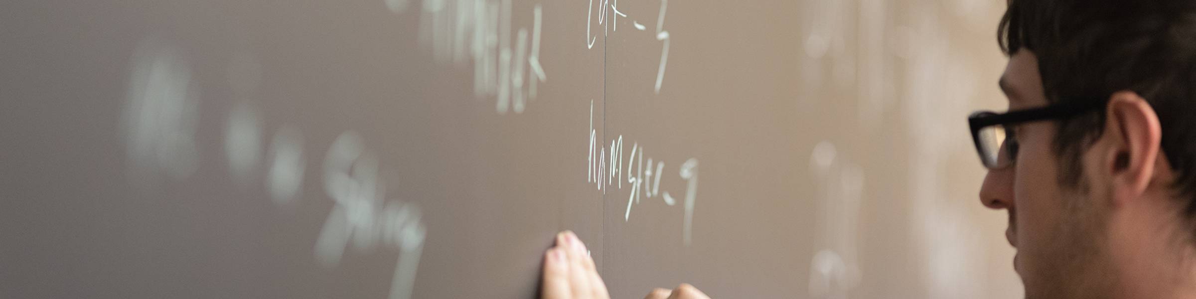 A computer science student writes out code on a blackboard.