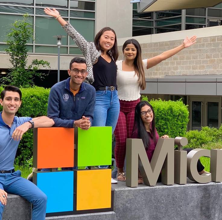 student interns stand on a Microsoft sign