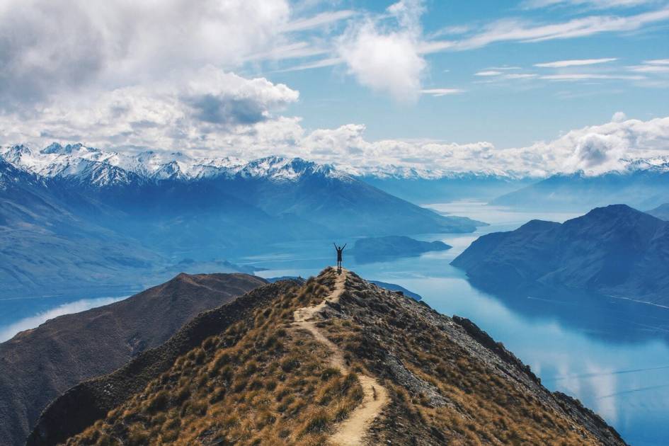 A photo of a college student at the top of a hill overlooking a lake in New Zealand.