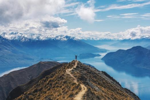 A photo of a college student at the top of a hill overlooking a lake in New Zealand.