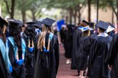 Students in caps and gowns walk to their commencement ceremony.
