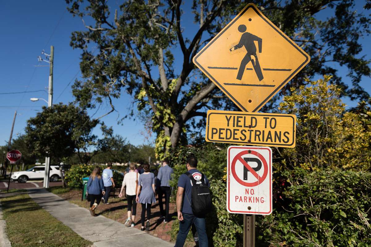 College students walking on the sidewalk past a yield to pedestrians sign.