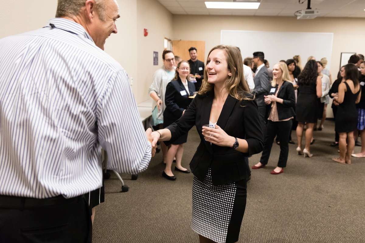 A college business student shaking the hand of and meeting a business owner.