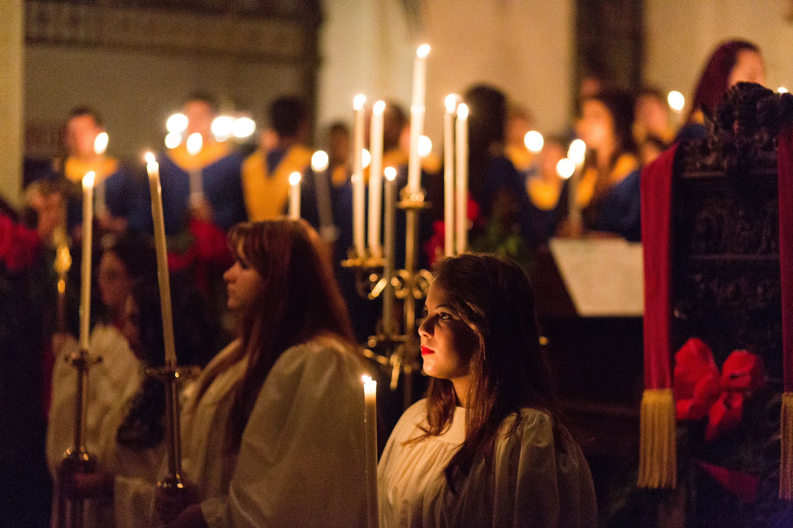 Choir members holding lit candles in a dimmed chapel