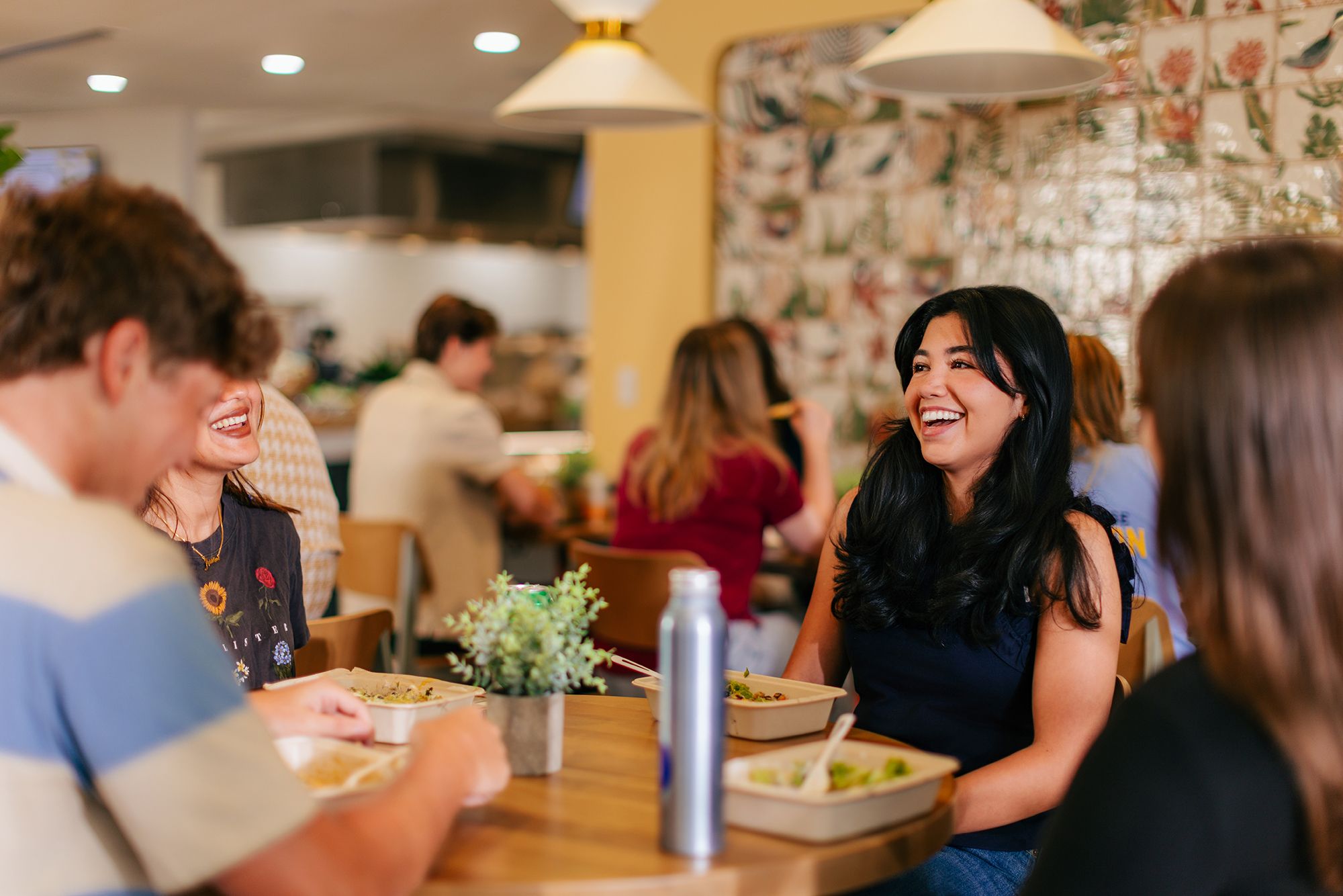 Friends laugh together while sharing a meal at a restaurant.