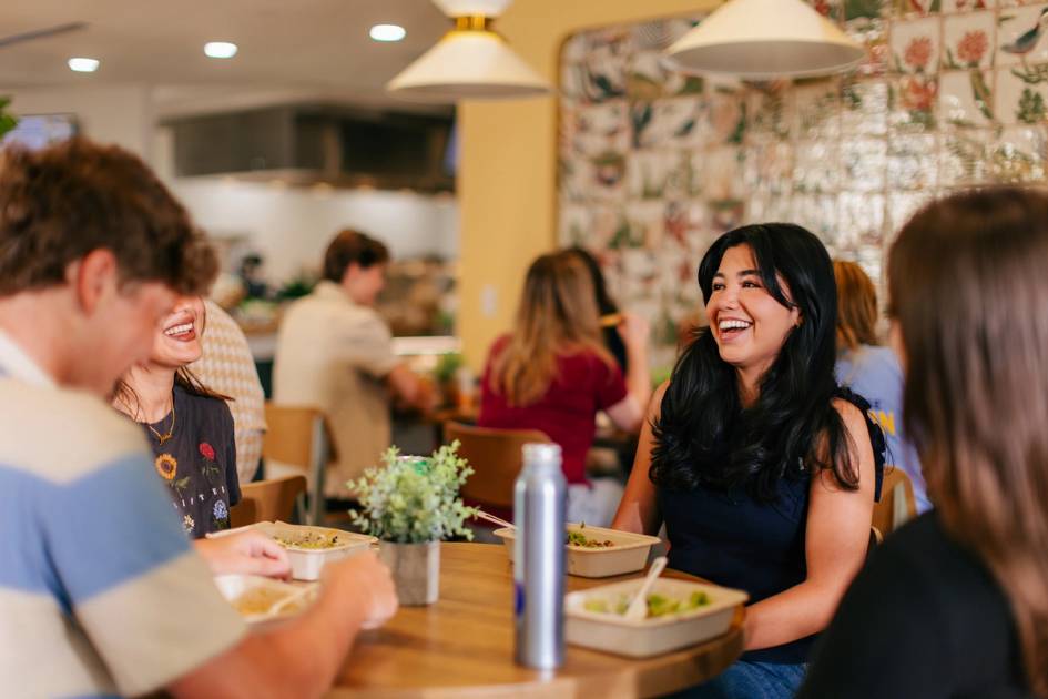 Friends laugh together while sharing a meal at a restaurant.
