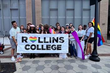 Members of Spectrum pose outside in downtown Orlando holding a Rollins College rainbow pride banner.
