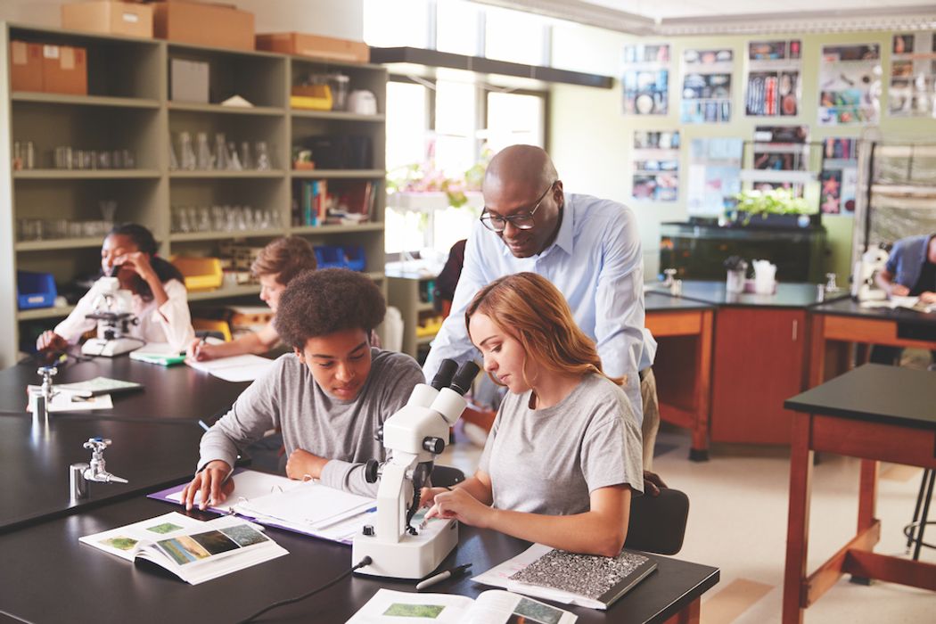 A teacher works with two young students in a science class.