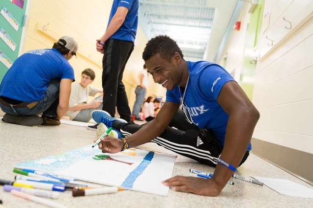 An African-American college student decorating a banner on the floor of a local Orlando elementary school.