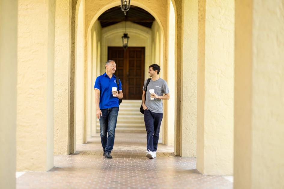 A Rollins professor and student wall through campus talking with coffee. 