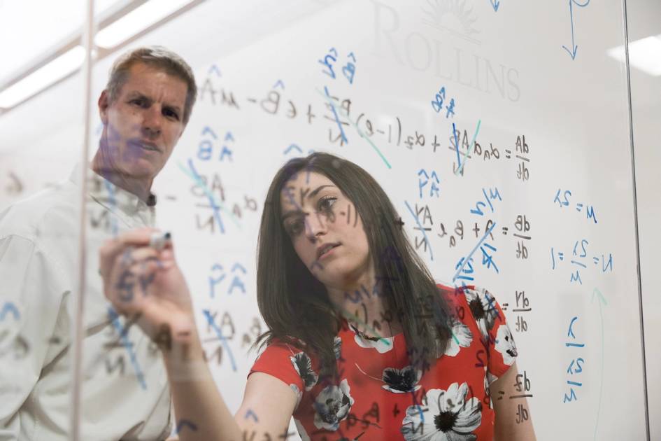 A professor and student work on a math equation.