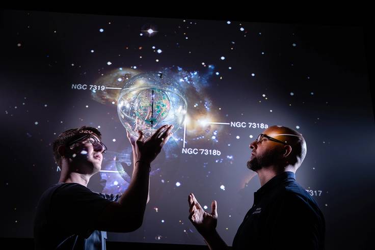Physics student and professor examine projected image of Earth against the universe.