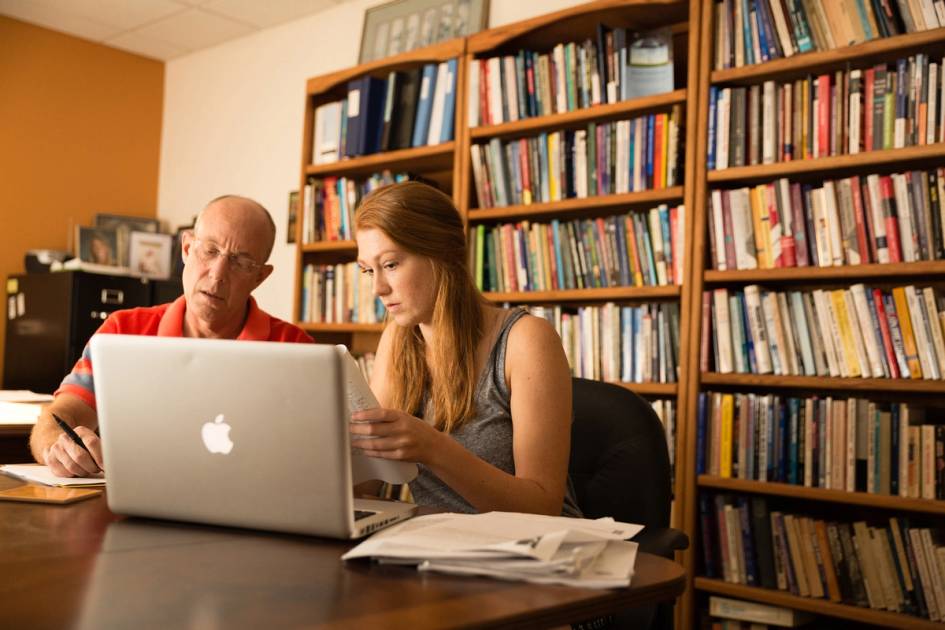 Rollins faculty member meets with a Rollins student in an office with a wall of books behind them