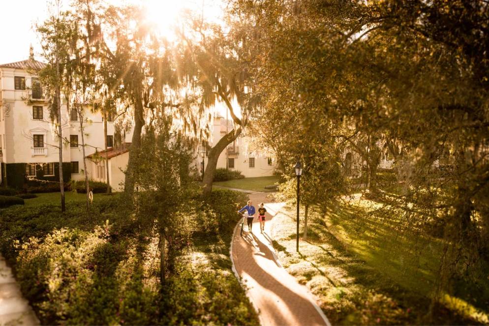 Students walking with bikes on campus under the oak trees.