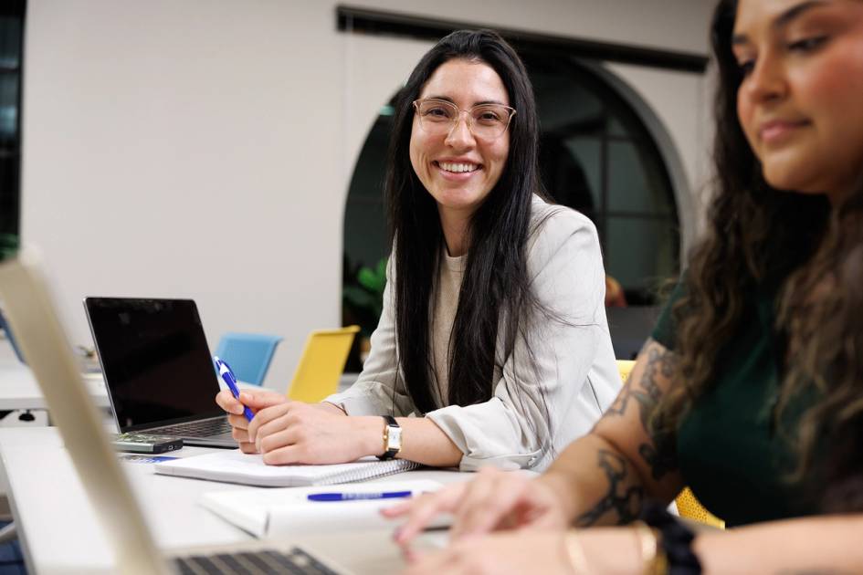 Smiling professional collaborating with colleague at laptops in modern office space