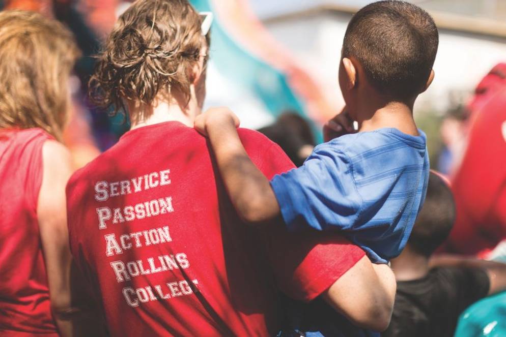 Rollins student wearing a SPARC Day shirt, carrying a child