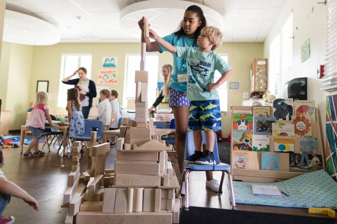 Rollins student working with preschool kids on a block building tower