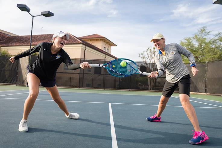 Mother-daughter tennis duo toss the ball around on the court.