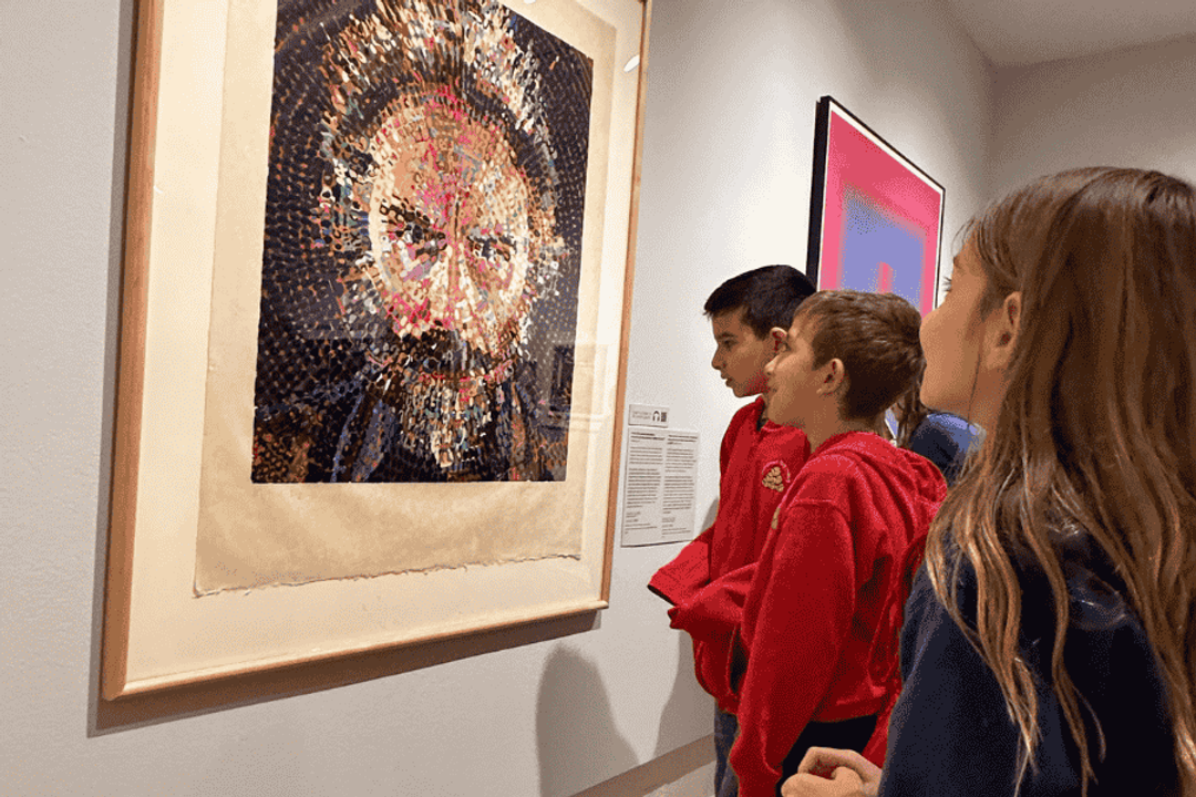 Children gather around an artwork of a bearded man's face