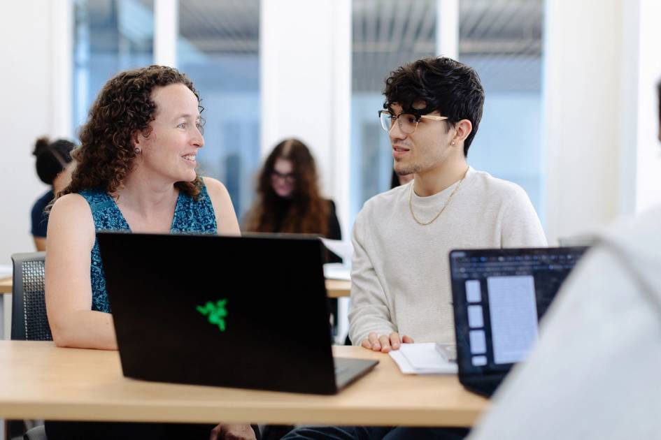 Instructor and student talking at laptops during a collaborative classroom session.