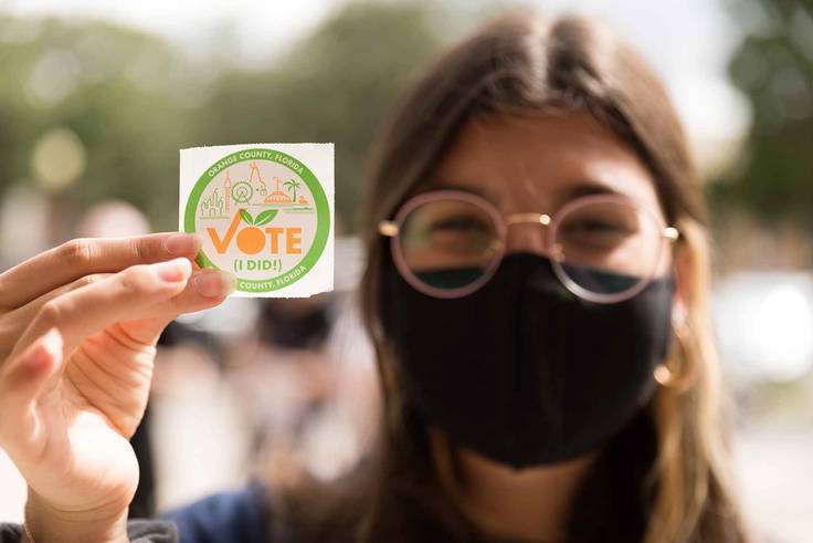 A student holds up an "I Voted" sticker