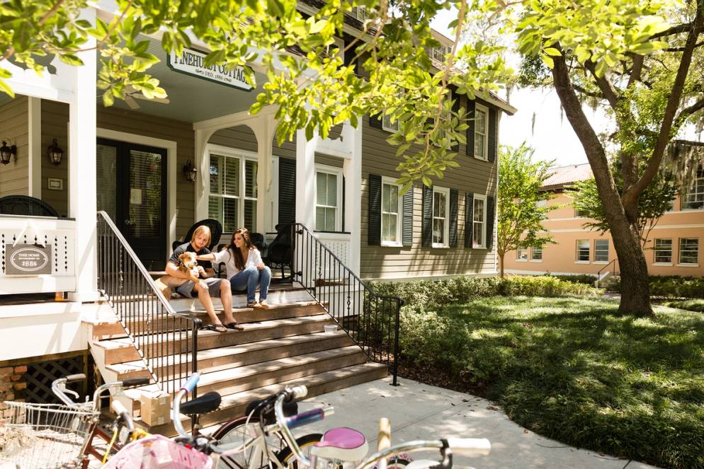 Students play with their dog on the porch of Pinehurst Cottage, the oldest building on campus.