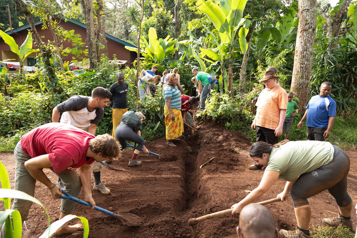 Students help Tanzanian villagers dig out a trench.