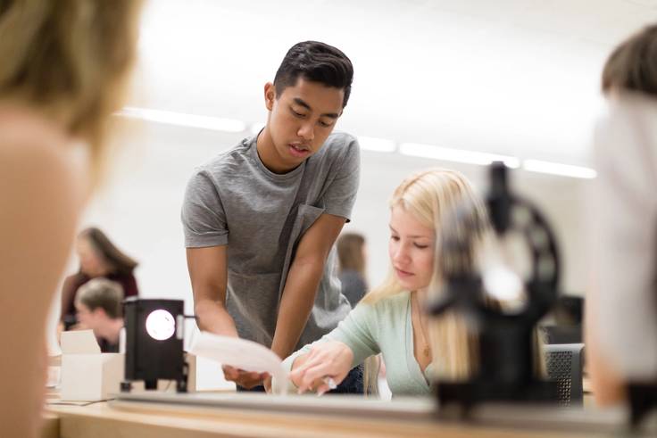 Peer mentor Jacob Battad helps a first-year student on an optics lab.