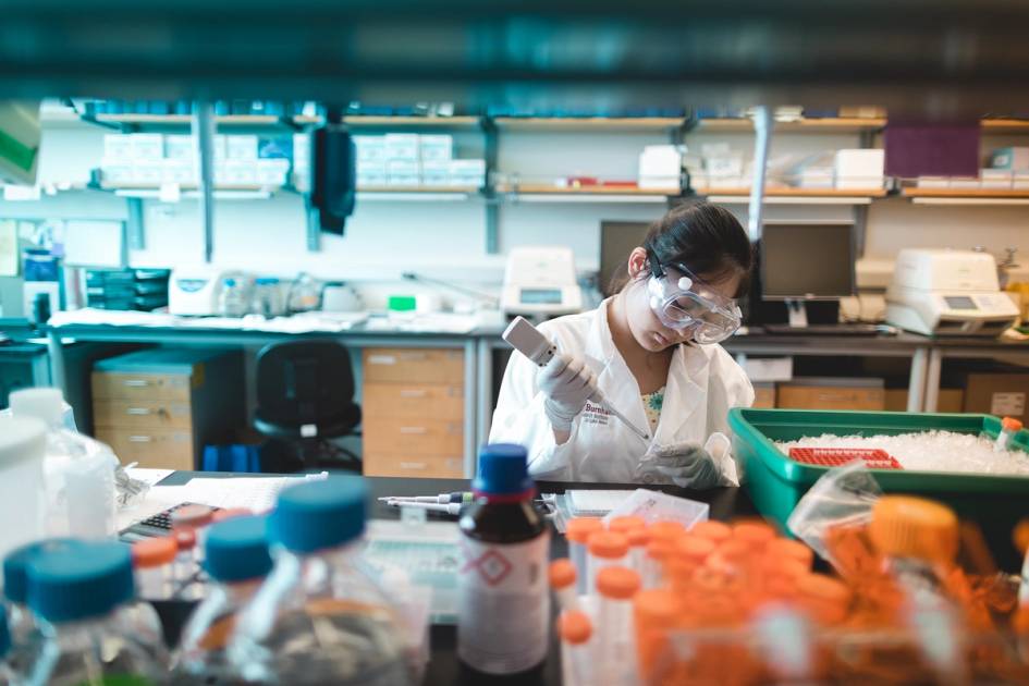 Rollins students interning in a graduate lab, with lab coat and eye protection on, student is conducting an experiment.