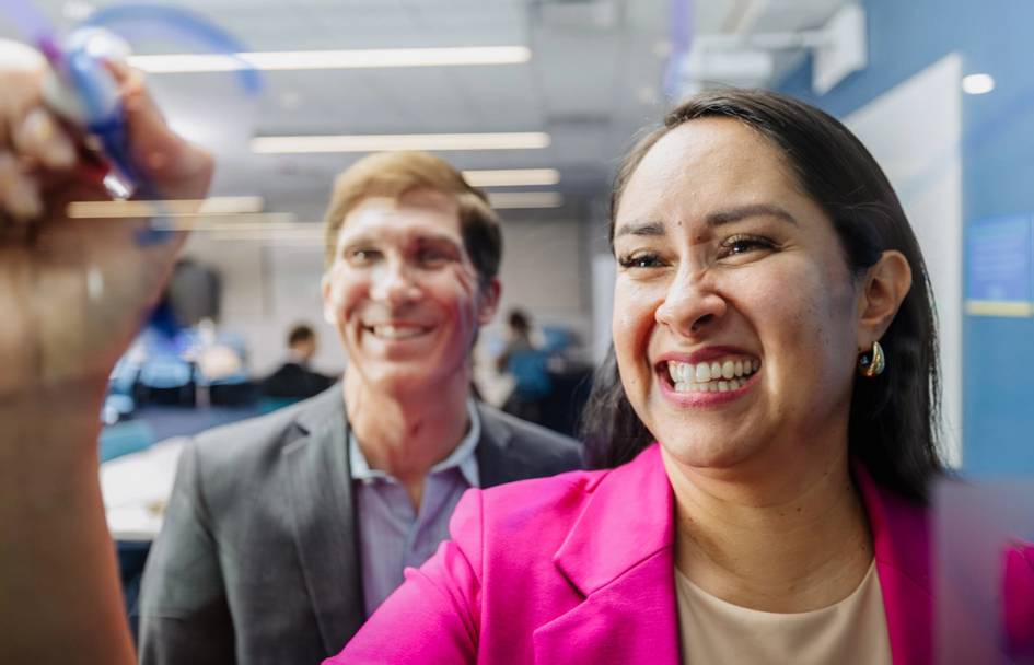 Smiling colleagues collaborate while writing ideas on a transparent office board.