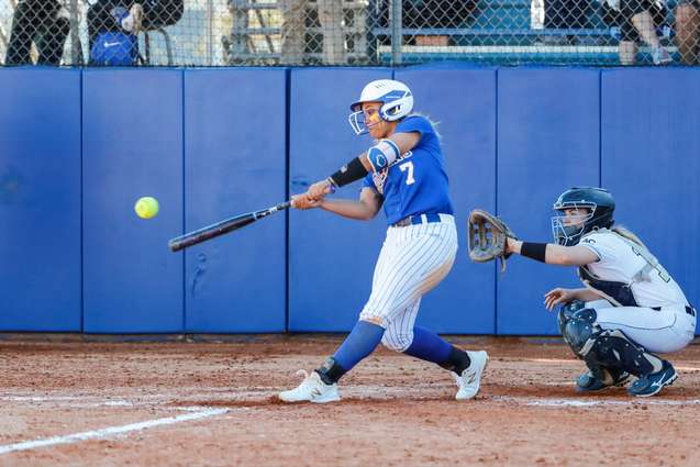 A softball player swinging and hitting a pitch over home plate.