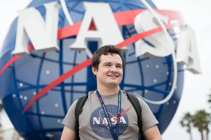 A student intern stands in front of a NASA sign at Kennedy Space Center.