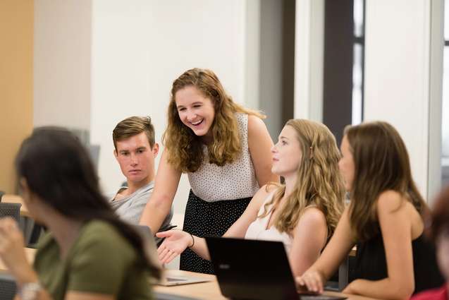 A liberal arts college professor looking at the computer screen of one of her students while smiling.