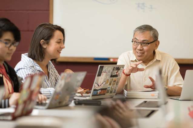 A college professor is sitting at a table addressing his students with their computers open.