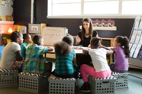 A teacher instructs a group of children seated around a table.
