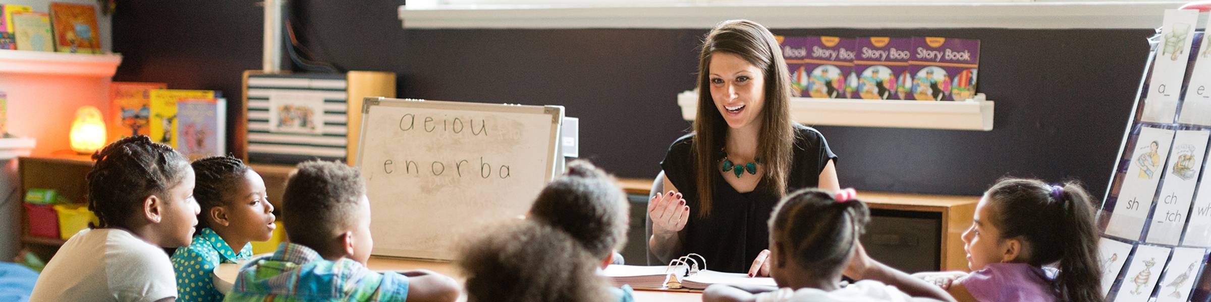 A teacher instructs a group of children seated around a table.