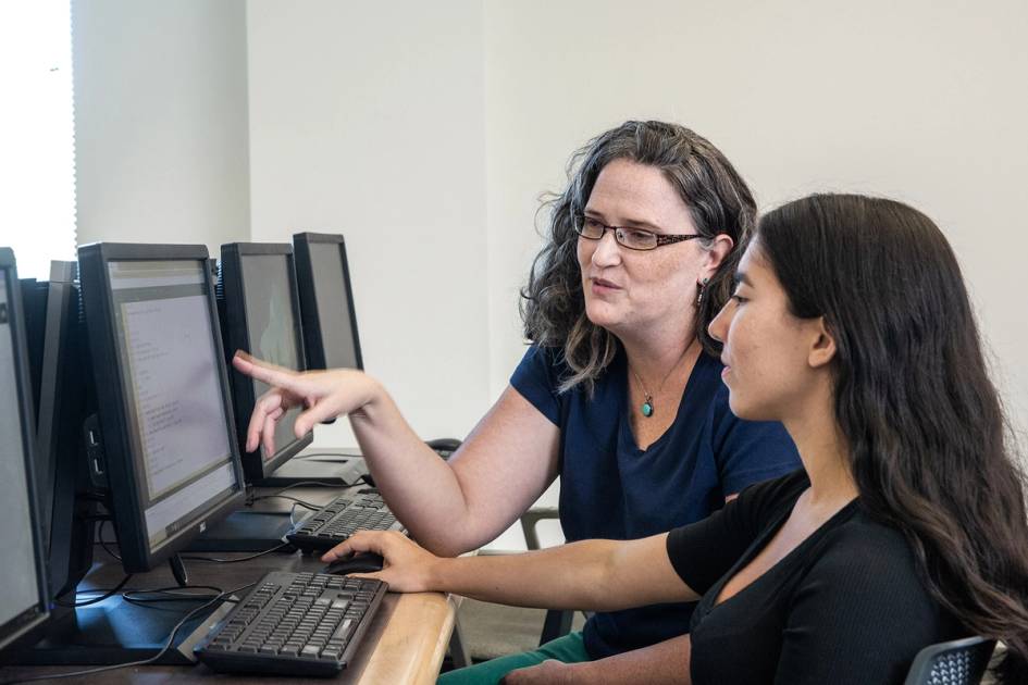 Instructor helping student with computer work in a classroom lab