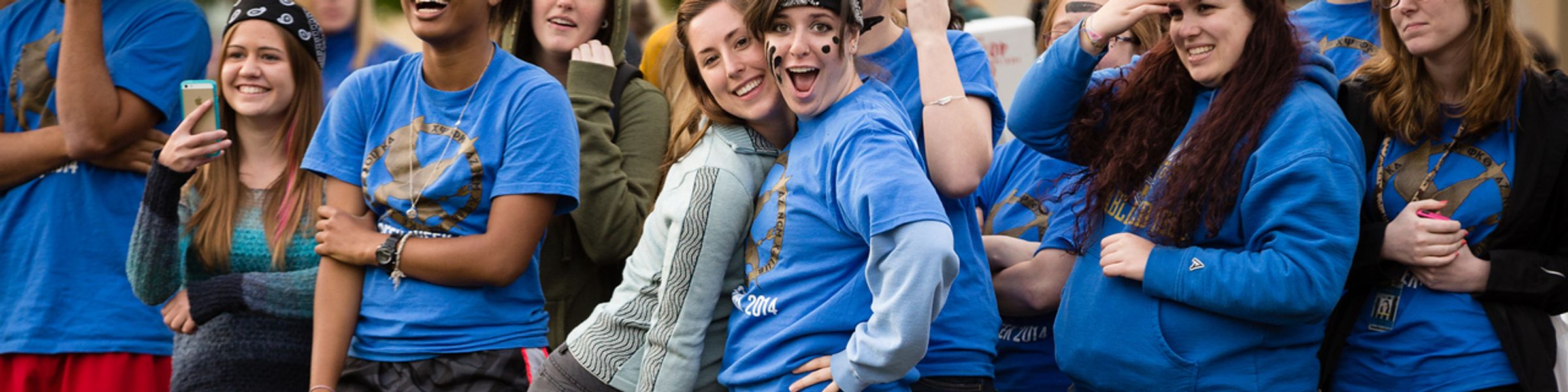 Sorority girls in blue t-shirts smiling, hugging, and looking at camera.