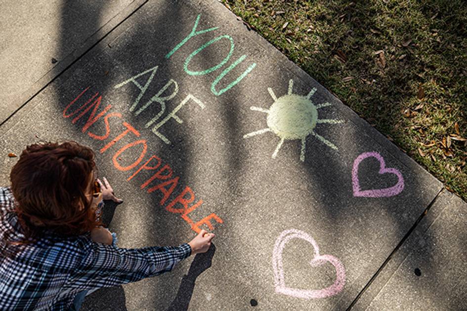 Student writing "You are unstoppable" on sidewalk with chalk