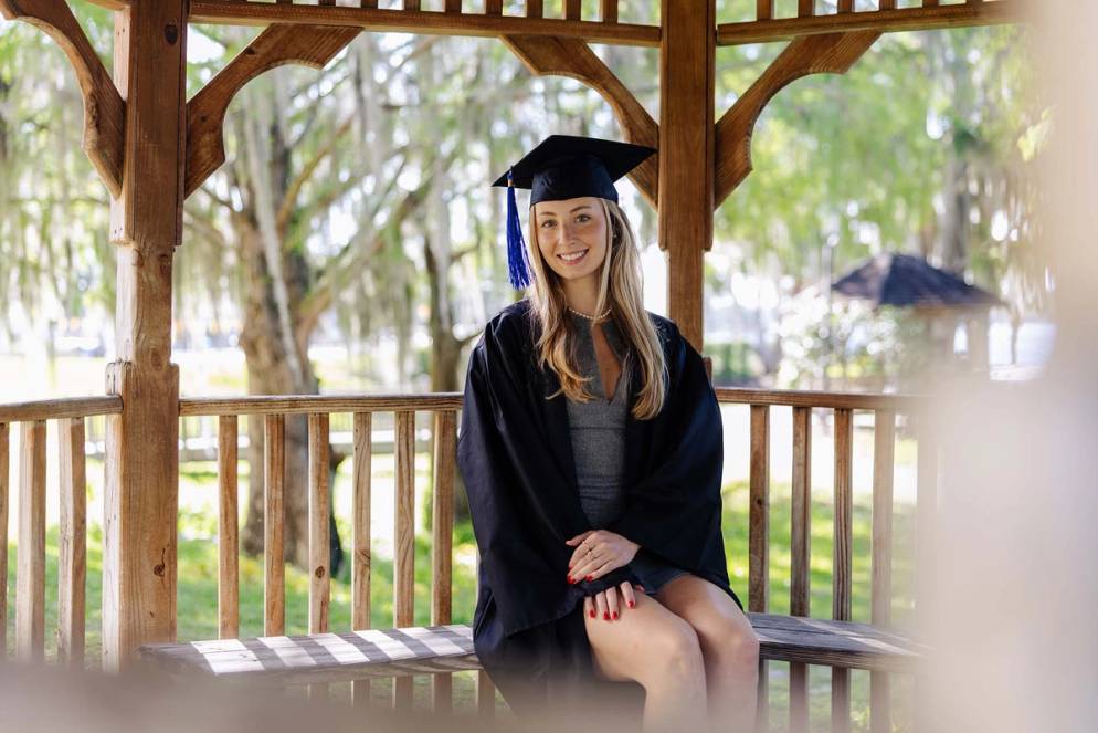 Nora Faunt Le Roy sits on a gazebo at Rollins College in her graduation regalia