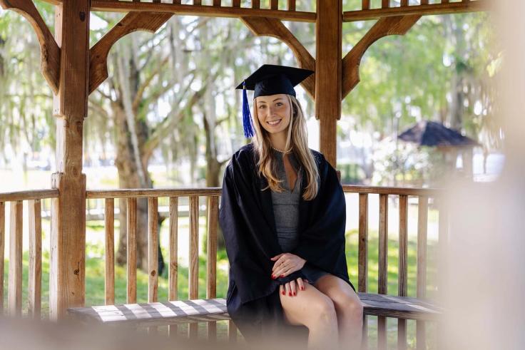 Nora Faunt Le Roy sits on a gazebo at Rollins College in her graduation regalia