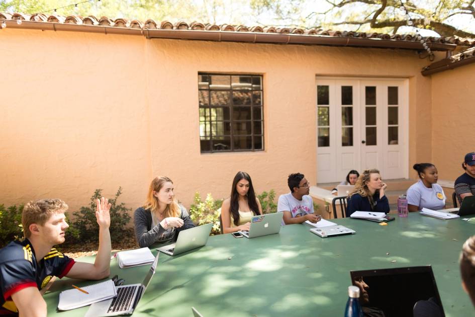 A group of Rollins students in an outdoor classroom discuss an assignment.