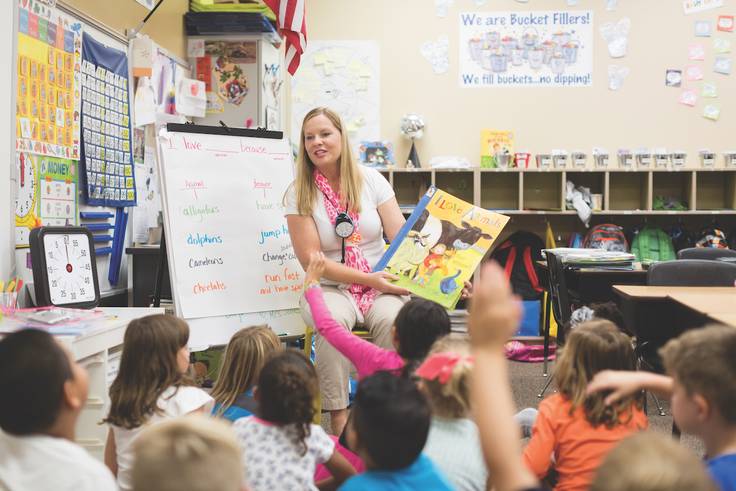A teacher reads to a class of seated elementary school students.