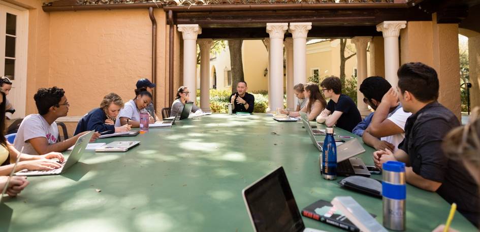 outside classroom with professor at the head of the table leading a conversation